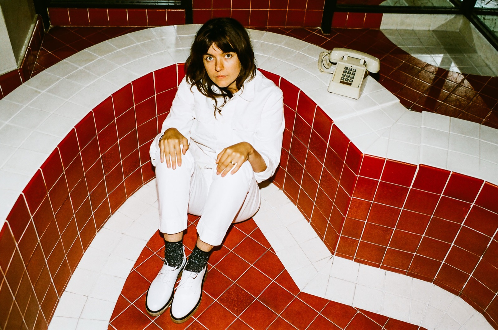 Courtney Barnett seated in a red-and-white tiled setting.